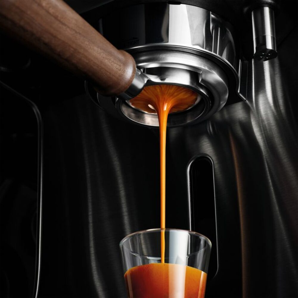 Espresso τη στιγμή της εκχύλισης: λεπτή καραμελένια ροή από γυμνό κλείστρο σε ιβουάρ φλιτζάνι με πλούσια φουντουκί crema, σε vintage μηχανή